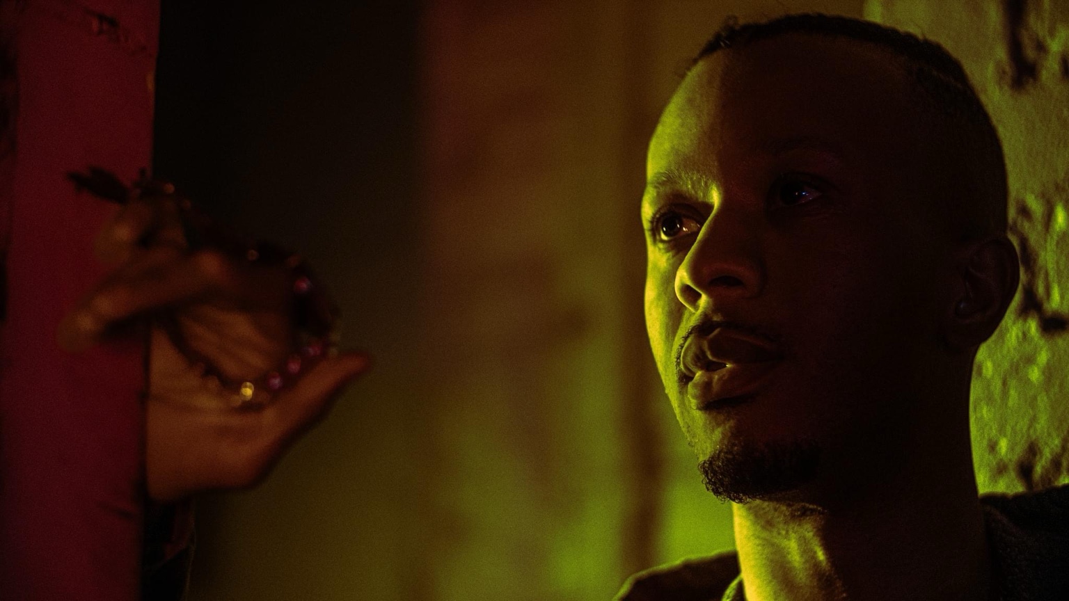 Keenan Laurino in alley with hand and beads in foreground